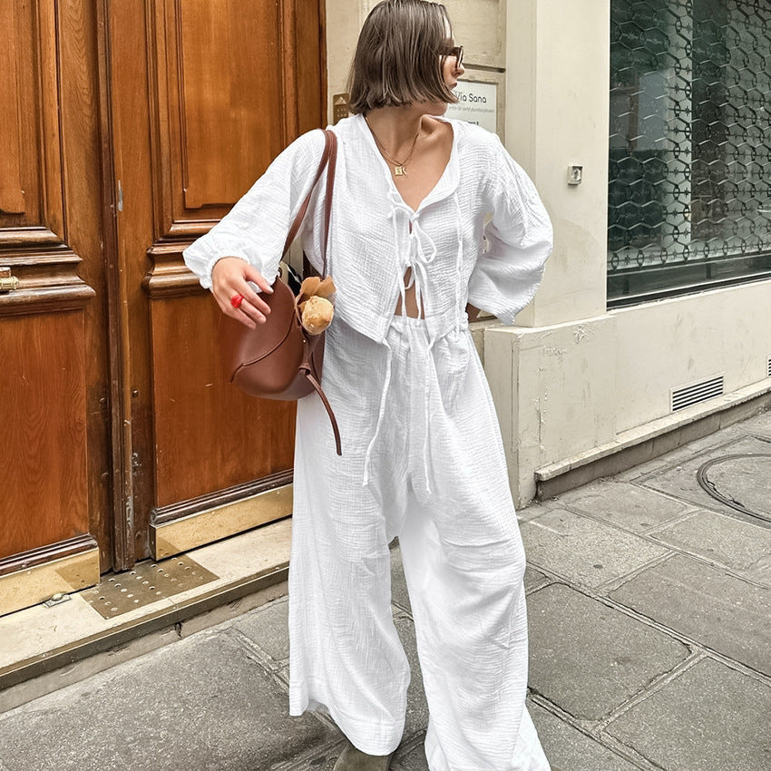 Frau in weißem Leinenanzug mit brauner Tasche und Teddybär, steht vor Holztür auf Pariser Straße. Modetrend, Sommeroutfit, Streetstyle.