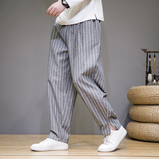 Graue gestreifte Herrenhose, lässig geschnitten, kombiniert mit weißen Sneakers. Modetrend, Herrenbekleidung, Freizeitlook.