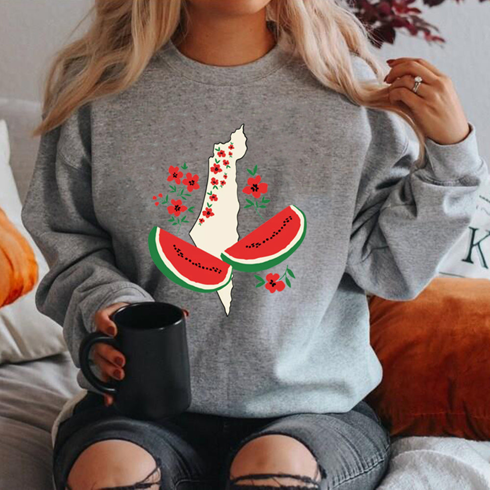 Frau in grauem Pullover mit Palästina-Karte, Wassermelonen- und Blumenmotiv, hält schwarze Tasse. Modetrend, Statement-Kleidung, gemütlicher Stil.