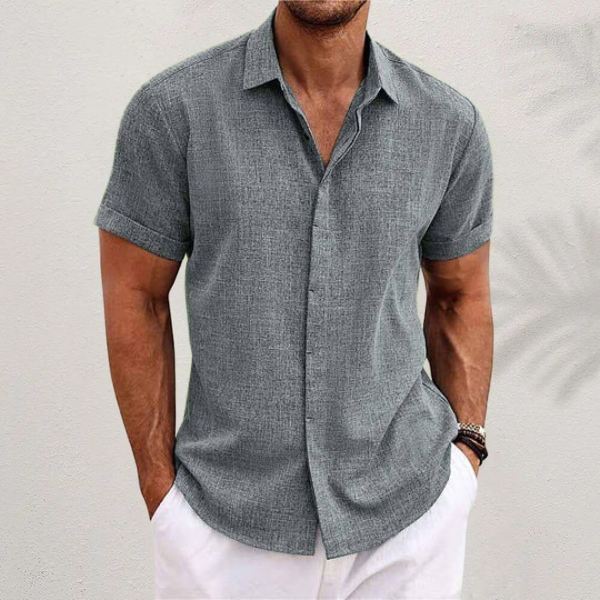 Mann in grauem Leinenhemd mit kurzen Ärmeln und weißer Hose vor neutralem Hintergrund. Sommermode, Herrenbekleidung, lässiger Stil.