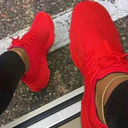 Rote Sneaker auf Asphalt, getragen von Person mit schwarzer Hose und goldener Knöchelkette. Modische Sportschuhe, urbaner Stil.