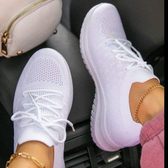 Weiße Sneaker auf Autositzen, getragen von Person mit rosa Hose und goldener Fußkette. Modische, bequeme Schuhe, ideal für Freizeit und Reisen.