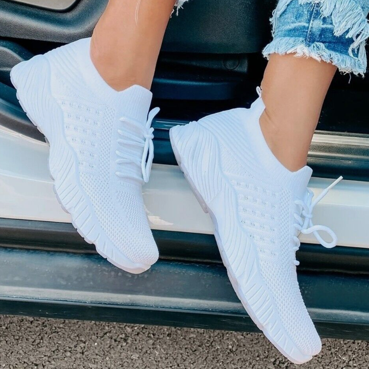 Weiße Sneaker mit Strickmuster, getragen von Person in zerrissenen Jeans, auf Autotür. Modische, bequeme Sportschuhe für Damen.