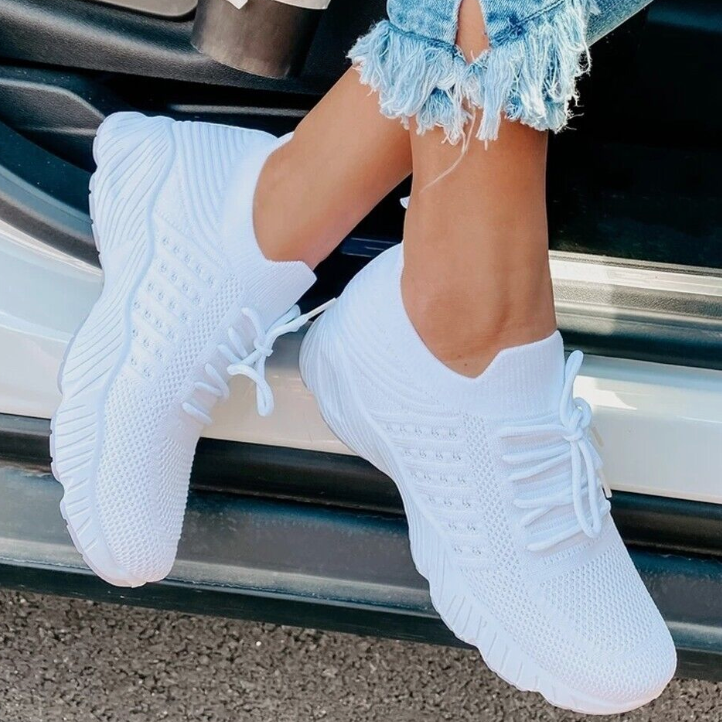Weiße Damen-Sneaker aus atmungsaktivem Strickmaterial, getragen von einer Person in zerrissenen Jeans, ideal für Freizeit und Sport.