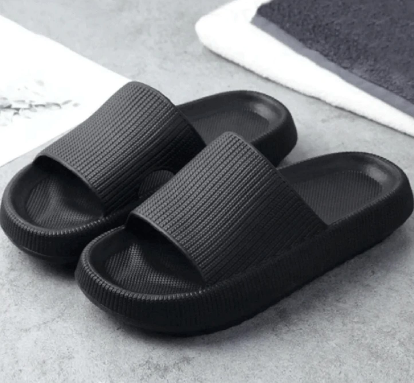 Schwarze Badeschlappen auf grauem Hintergrund, rutschfest und bequem, ideal für Badezimmer oder Strand. Modische und praktische Hausschuhe.