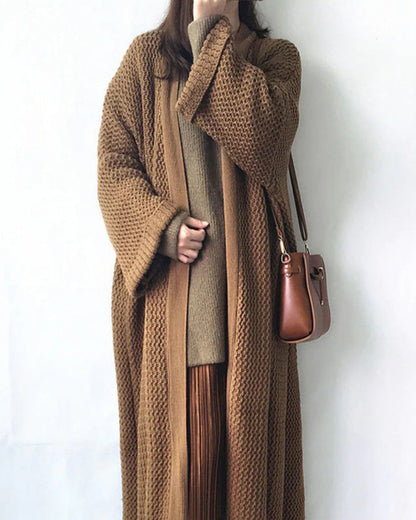 Frau in langem, braunem Strickmantel mit passender Tasche. Modetrend Herbst/Winter, gemütlicher Look, stilvolle Damenbekleidung.