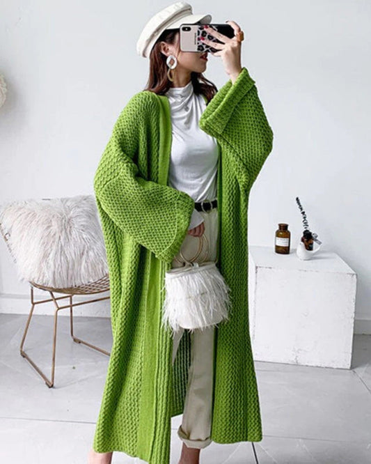 Frau in grünem Strickmantel, weißem Hut und Federhandtasche, posiert mit Smartphone. Modetrend, Herbstmode, Streetstyle, Damenbekleidung.