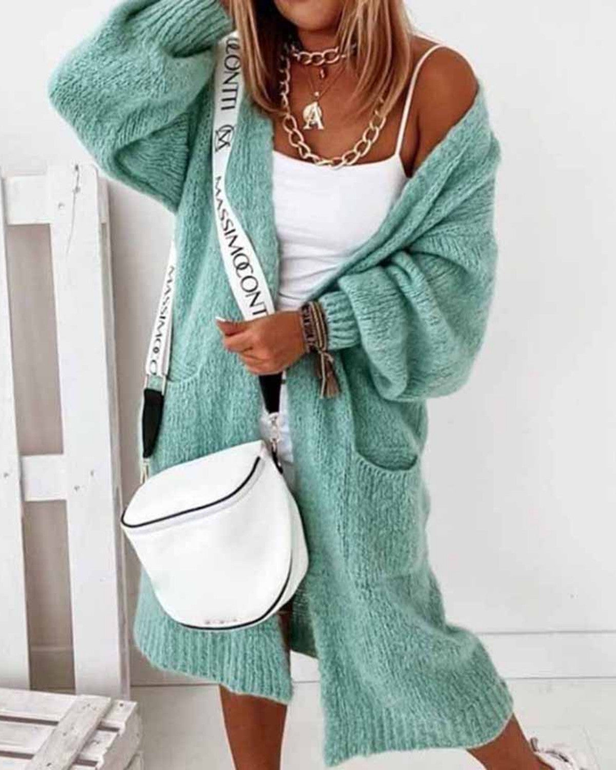 Frau in mintgrünem Strick-Cardigan, weißem Top und Shorts, trägt weiße Umhängetasche. Modetrend, lässiger Look, Sommeroutfit.