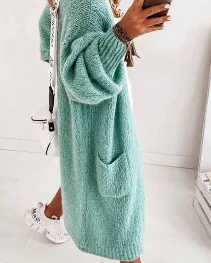 Frau in mintgrünem Strickkleid mit Taschen, hält Smartphone, trägt weiße Sneakers und weiße Umhängetasche. Modetrend, lässiger Stil.