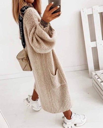 Frau in beigem Strickkleid mit langen Ärmeln, weißen Sneakers und beiger Umhängetasche, hält Smartphone. Modetrend, Herbstmode, Streetstyle.