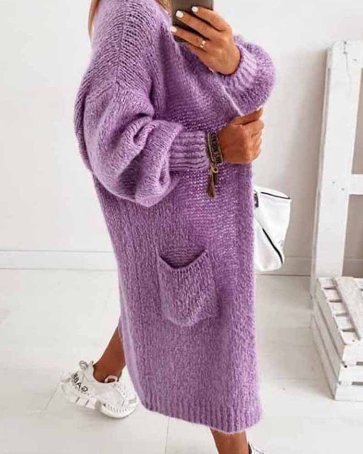 Frau in lila Strickkleid mit Tasche, weiße Sneakers, weiße Handtasche, modisch, gemütlich, Herbstmode, lässiger Stil, Innenraum.