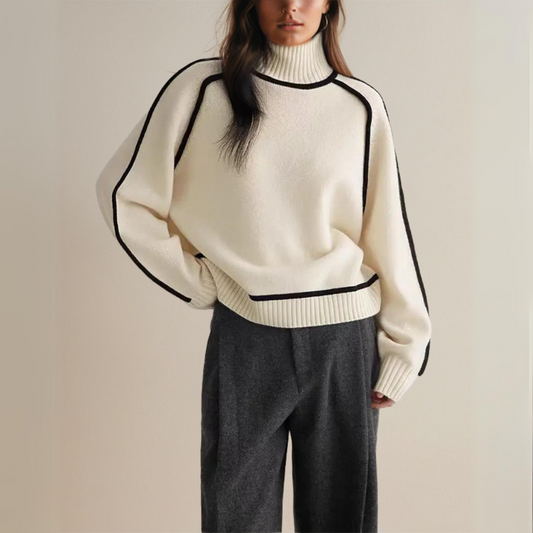 Frau in cremefarbenem Rollkragenpullover mit schwarzen Akzenten und grauer Hose. Modetrend, Herbstmode, Damenbekleidung, eleganter Look.