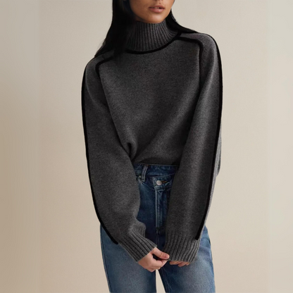 Frau trägt grauen Rollkragenpullover und blaue Jeans, modischer Herbst-Look, gemütlicher Strick, lässiger Stil, Damenmode, Streetwear-Trend.