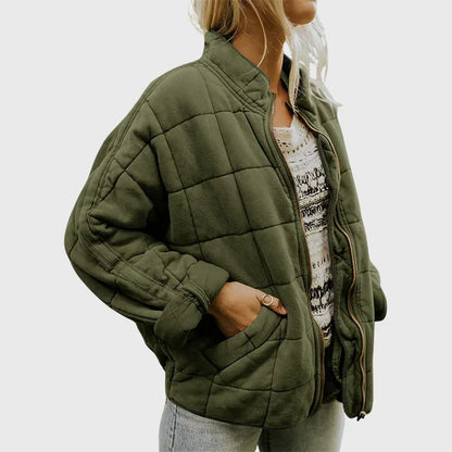 Frau in olivgrüner Steppjacke, lässig offen getragen, mit gemustertem Oberteil und Jeans. Modetrend, Herbstmode, Damenjacke, Streetstyle.