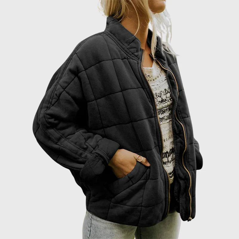 Frau in schwarzer, gesteppter Jacke mit Reißverschluss, weißem gemustertem Oberteil und blauer Jeans. Modetrend, Damenbekleidung, Herbstmode.