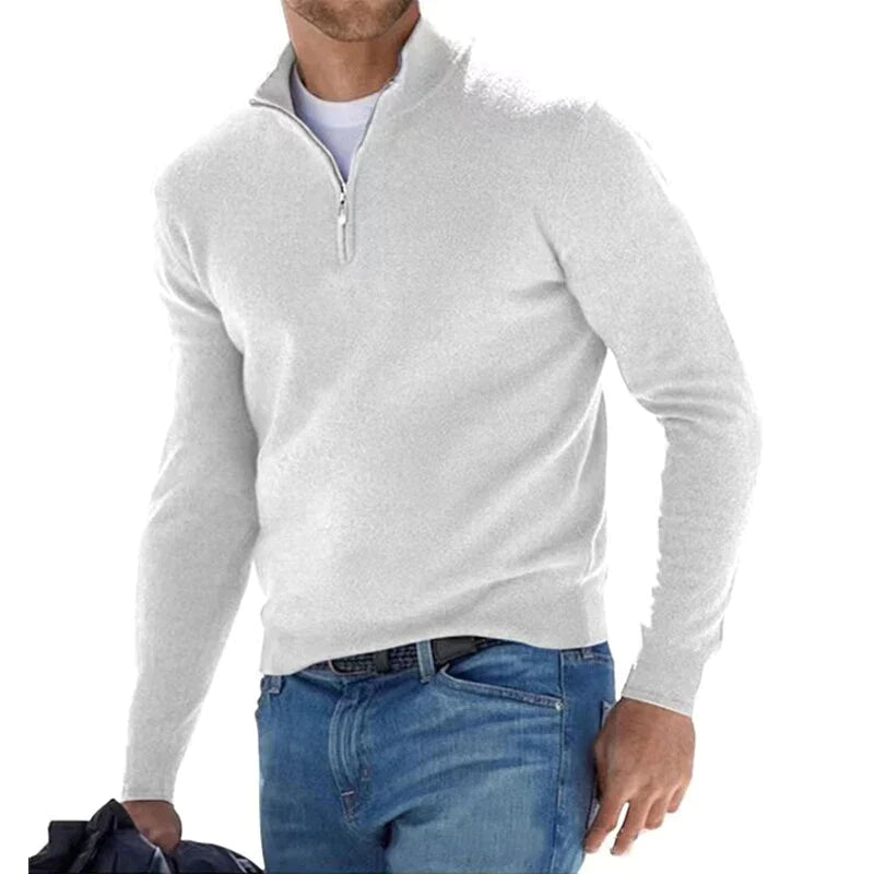 Mann in weißem Pullover mit Reißverschluss und blauer Jeans, hält eine Jacke. Modischer Herren-Look, Freizeitkleidung, stilvoll und bequem.
