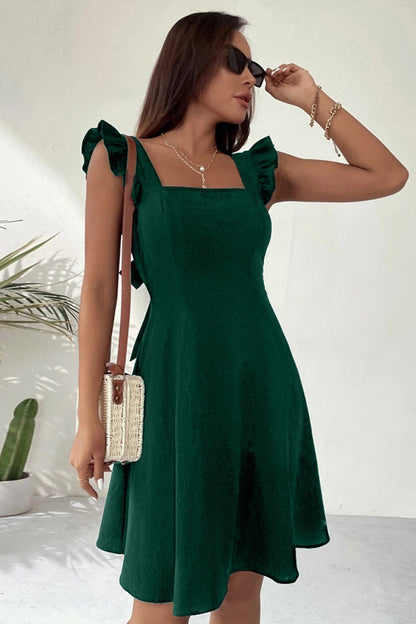 Frau in grünem Sommerkleid mit Rüschenärmeln, Sonnenbrille und Strohtasche. Elegante Mode, Sommeroutfit, Damenbekleidung.