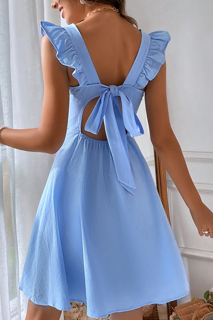 Frau in hellblauem Sommerkleid mit Rückenausschnitt und Schleife, Rüschenärmeln, stehend vor einem Fenster. Elegantes, luftiges Design.