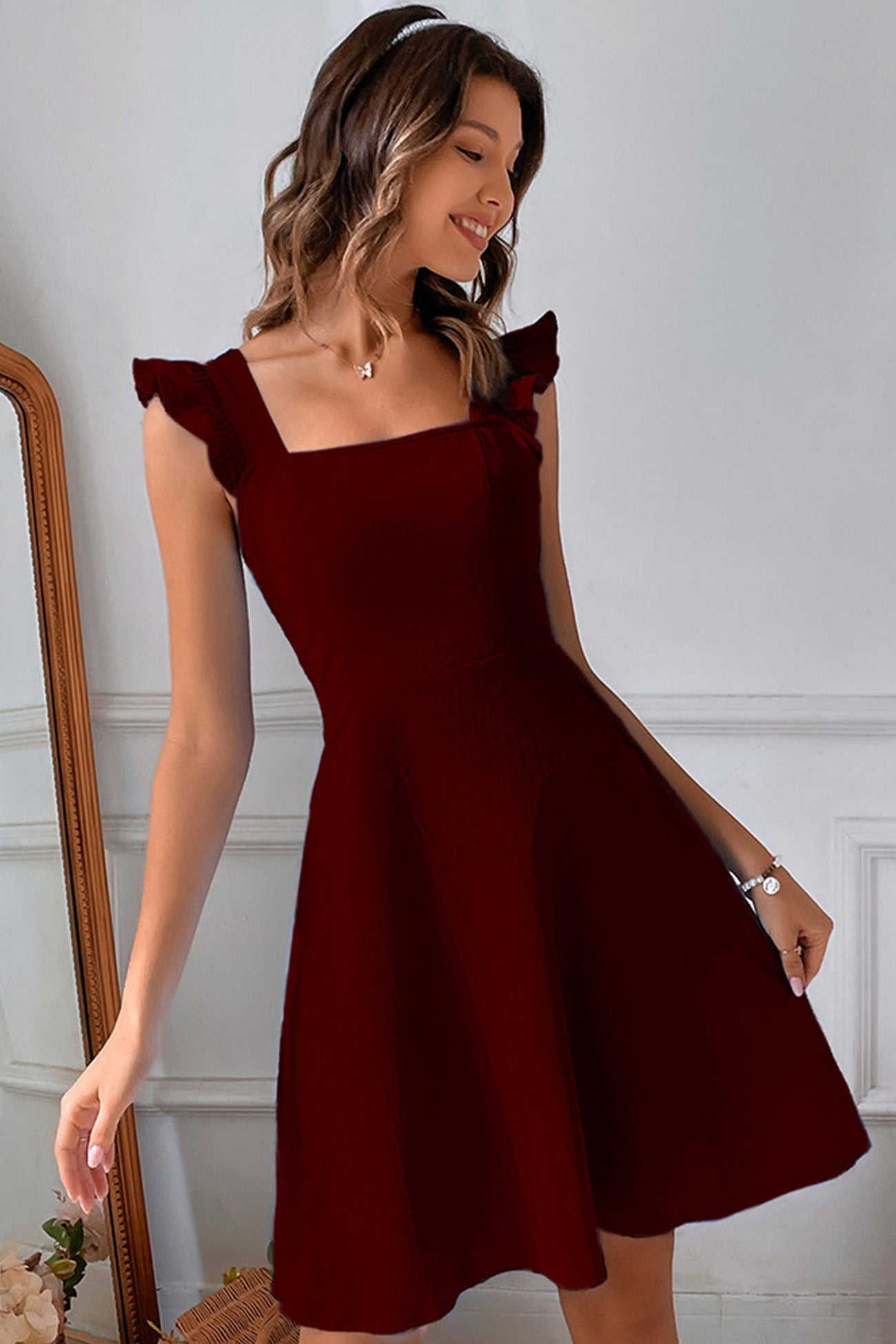 Frau in elegantem, weinrotem Kleid mit Rüschenärmeln, lächelnd vor einem Spiegel. Perfektes Outfit für Abendveranstaltungen und Partys.