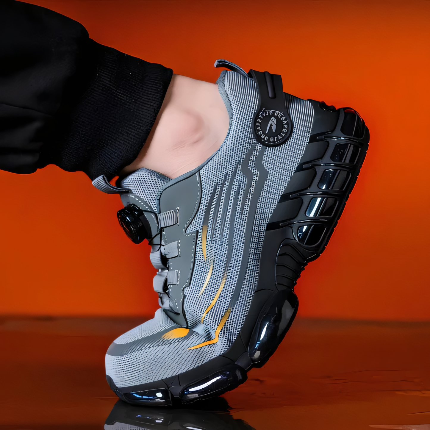 Grauer Sportschuh mit schwarzer Sohle und gelben Akzenten auf reflektierendem Untergrund vor orangefarbenem Hintergrund. Innovatives Design, modern.