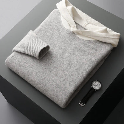 Grauer Kaschmirpullover mit weißem Kragen, gefaltet auf grauem Tisch, neben einer eleganten Armbanduhr. Luxuriöse Mode, stilvolle Accessoires.