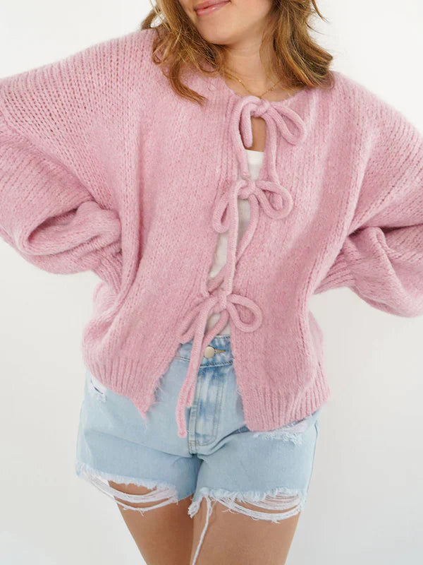 Frau trägt rosa Strickjacke mit Schleifen, kombiniert mit zerrissenen Jeansshorts. Modetrend, lässiger Look, Damenmode, Strickjacke, Sommeroutfit.