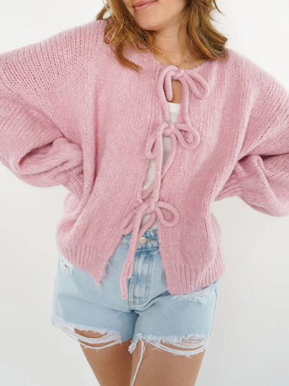 Frau trägt rosa Strickjacke mit Schleifen, kombiniert mit zerrissenen Jeansshorts. Modetrend, lässiger Look, Damenmode, Strickjacke, Sommeroutfit.