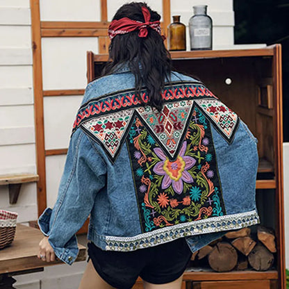 Frau mit bunter, bestickter Jeansjacke, ethnisches Muster, Blumenmotiv, Outdoor-Szene, modische Damenbekleidung, Boho-Stil, Rückansicht.