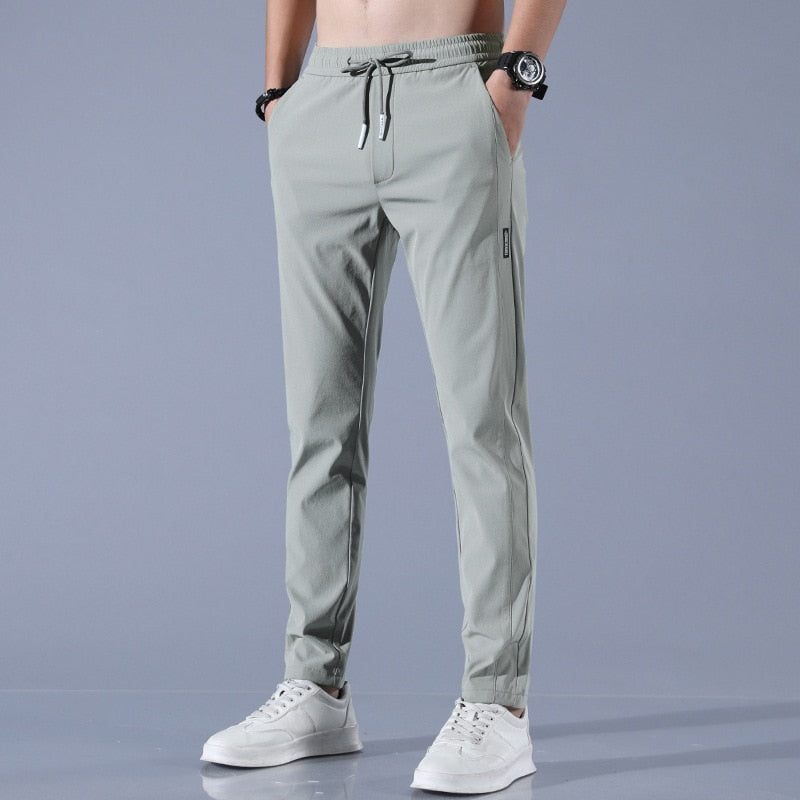 Graue Herren-Jogginghose mit Kordelzug, Taschen und weißem Sneaker. Sportliche Freizeitmode, ideal für Fitness und Alltag.