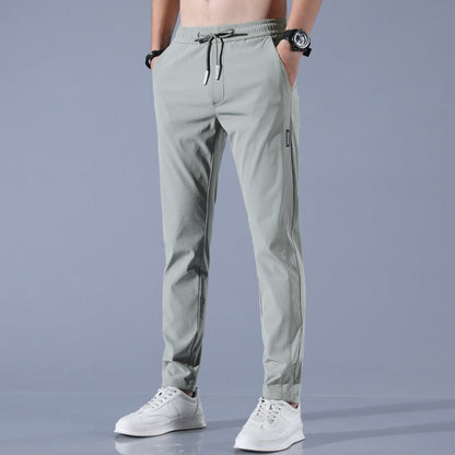 Graue Herren-Jogginghose mit Kordelzug, Taschen und weißem Sneaker. Sportliche Freizeitmode, ideal für Fitness und Alltag.