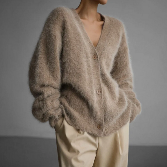 Frau trägt flauschigen, beigen Strick-Cardigan mit Knöpfen und weiten Ärmeln, kombiniert mit hellen, weiten Hosen. Elegante, gemütliche Mode.