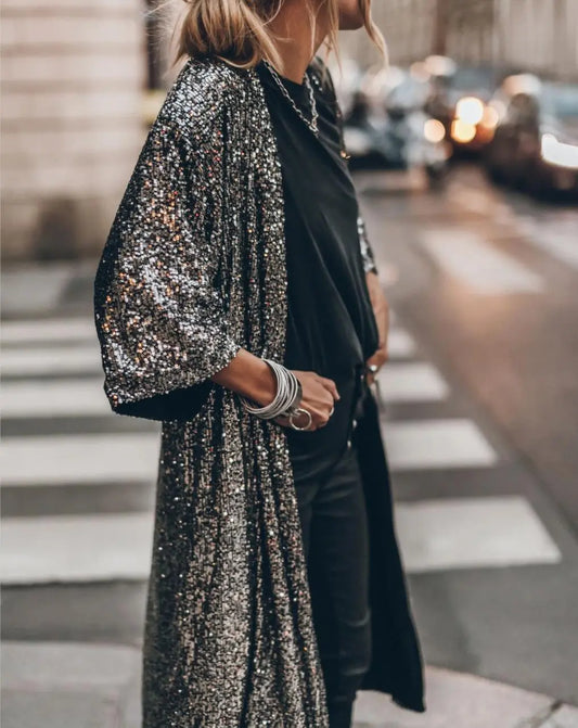 Frau in glitzerndem Paillettenmantel auf Straße, modisches Outfit, Abendmode, stilvolle Kleidung, urbane Kulisse, trendige Accessoires.