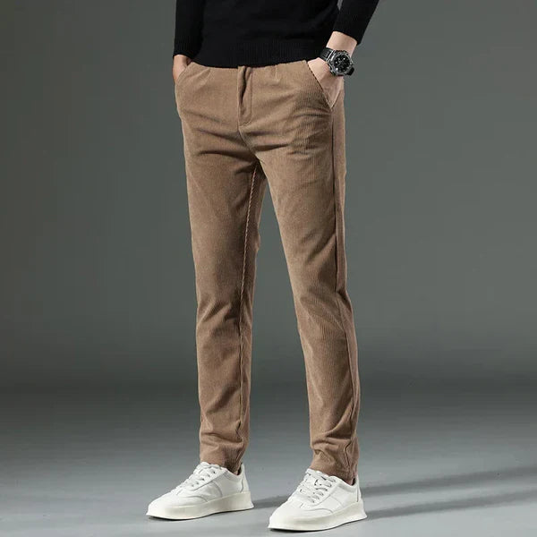 Braune Cordhose für Herren, kombiniert mit weißem Sneaker und schwarzem Pullover. Modischer, lässiger Look, ideal für Herbst und Winter.