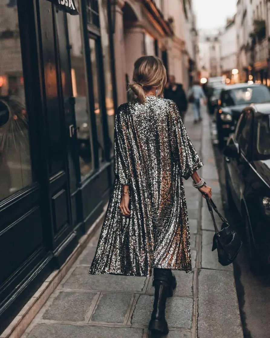 Frau in glitzerndem Paillettenmantel geht auf Pariser Straße, trägt schwarze Stiefel und Handtasche. Modestil, Straßenmode, Paris.