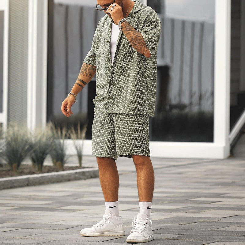 Mann in grünem Sommeranzug mit geometrischem Muster, weißen Sneakers und Socken. Trendige Herrenmode, lässiger Stil, urbaner Hintergrund.