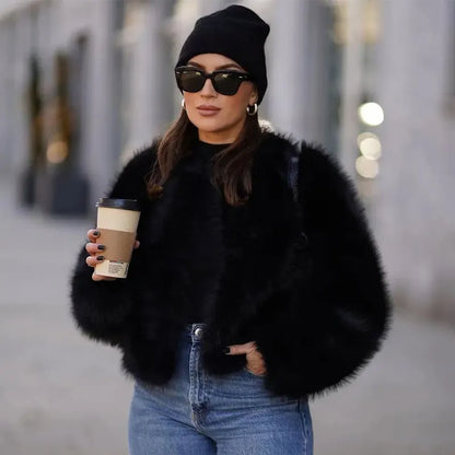 Frau in schwarzer Felljacke, blauer Jeans und Mütze hält Kaffeebecher. Modetrend, Winteroutfit, Streetstyle, Sonnenbrille, urbaner Look.