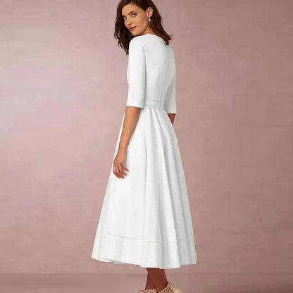 Frau in elegantem, weißem Kleid mit halblangen Ärmeln, stehend vor rosa Hintergrund. Mode, Damenbekleidung, Abendkleid, stilvoll.