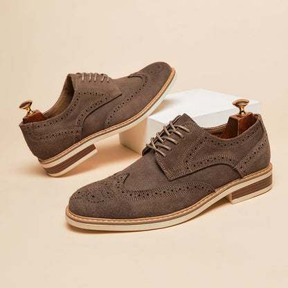 Braune Herren-Brogues aus Wildleder mit Lochmuster, flachem Absatz und Schnürung, auf beigem Hintergrund. Elegante Herrenschuhe, stilvoll und modern.