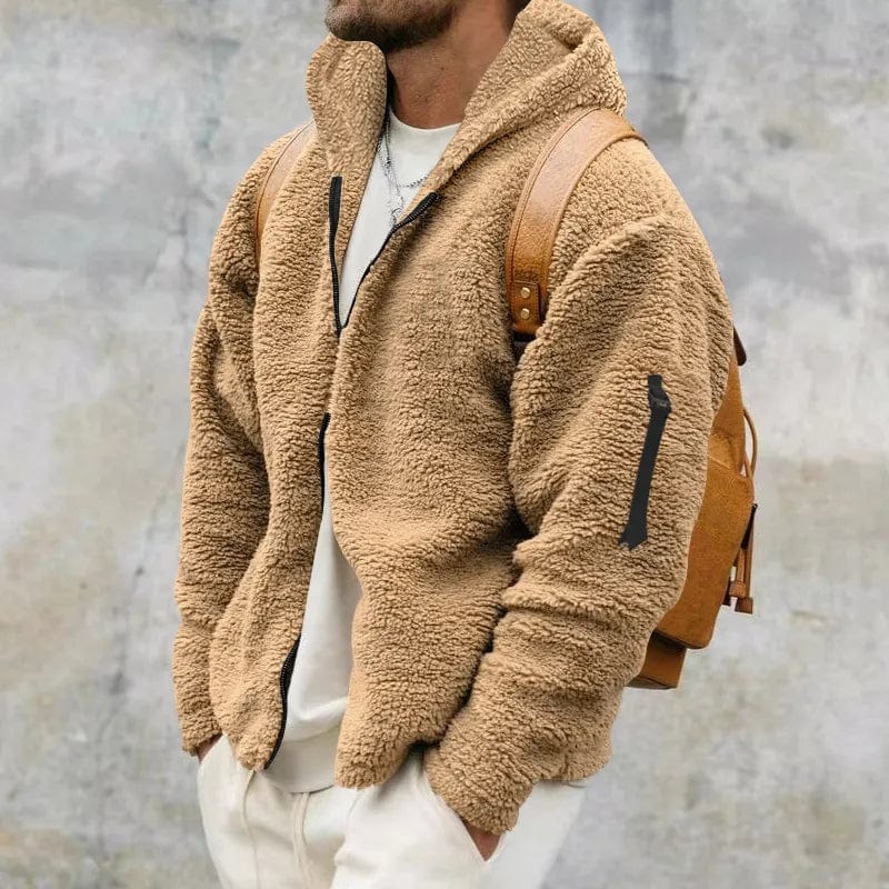 Mann in beiger Teddyfleece-Jacke mit Reißverschluss und braunem Rucksack vor grauem Hintergrund. Modetrend, Herbstmode, Herrenbekleidung.