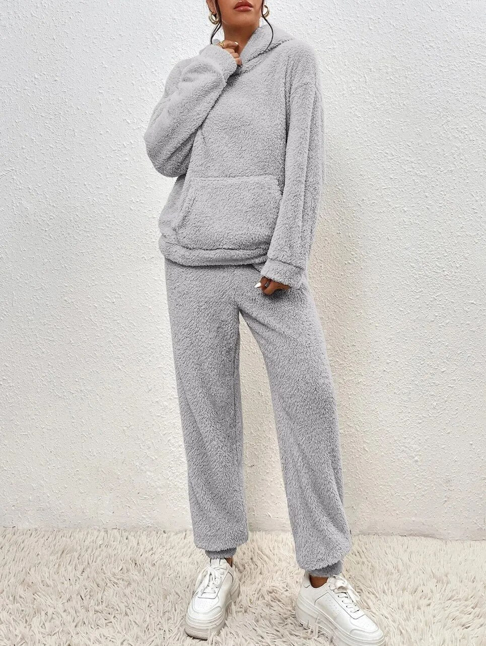 Grauer Fleece-Hoodie und Jogginghose Set, gemütliche Damen-Loungewear, weiches Material, modisch, ideal für Herbst und Winter, kombiniert mit weißen Sneakers.