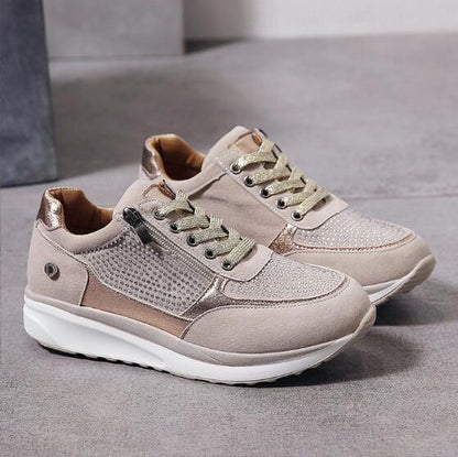 Beige Damen-Sneaker mit goldenen Akzenten, Reißverschluss und Schnürsenkeln auf grauem Hintergrund. Modische Freizeitschuhe für Damen.