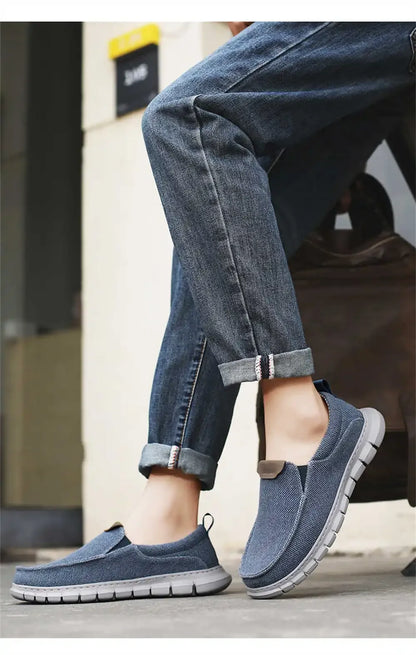 Jeans und blaue Freizeitschuhe auf Gehweg. Bequeme, atmungsaktive Slip-On-Sneaker für Herren. Perfekt für lässige Outfits und Spaziergänge.