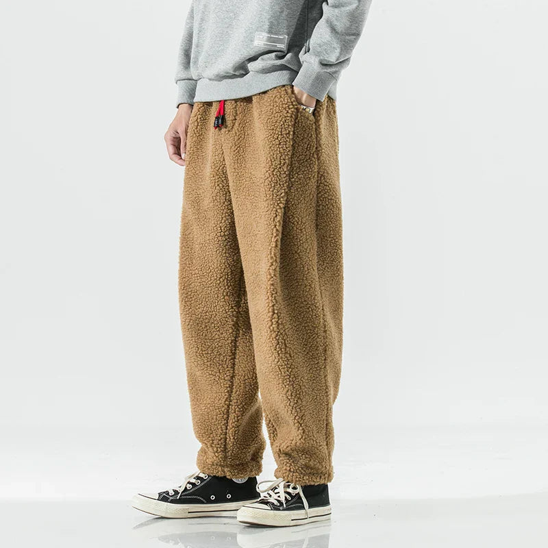 Person trägt braune Fleece-Jogginghose, kombiniert mit grauem Sweatshirt und schwarzen Sneakers. Bequeme, warme Freizeitmode für Herren.