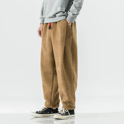 Person trägt braune Fleece-Jogginghose, kombiniert mit grauem Sweatshirt und schwarzen Sneakers. Bequeme, warme Freizeitmode für Herren.