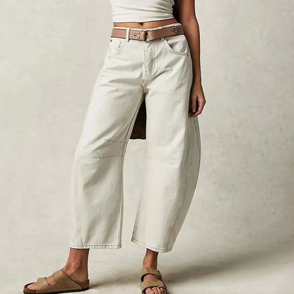 Frau trägt weiße, weite Jeans mit braunem Gürtel und Sandalen. Modetrend, lässiger Stil, Damenbekleidung, Sommeroutfit.