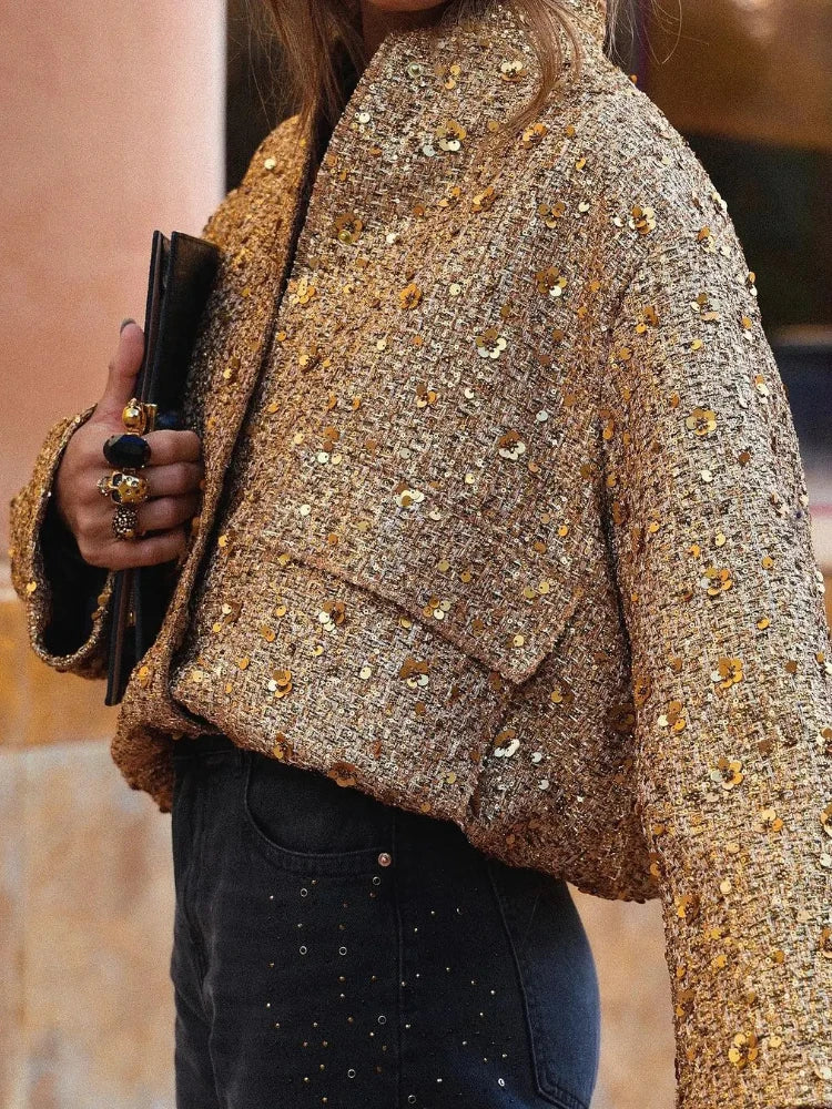 Frau in goldener Paillettenjacke hält schwarze Clutch. Modetrend, glamouröser Look, elegantes Outfit, Abendmode, stilvolle Damenbekleidung.
