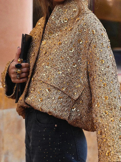 Frau in goldener Paillettenjacke hält schwarze Clutch. Modetrend, glamouröser Look, elegantes Outfit, Abendmode, stilvolle Damenbekleidung.