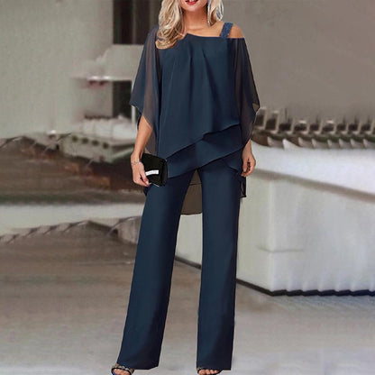 Elegante Frau in dunkelblauem, schulterfreiem Hosenanzug mit Clutch, stehend in modernem, minimalistischem Innenraum.