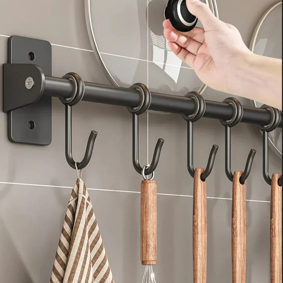 Hand greift nach Topfdeckel an Wandhakenleiste mit Küchenutensilien und Geschirrtuch, moderne Küchendekoration, platzsparende Aufbewahrungslösung.