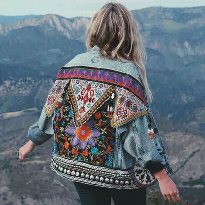 Frau mit bunter, bestickter Jeansjacke vor Berglandschaft. Boho-Stil, Vintage-Mode, Outdoor-Abenteuer, trendige Damenbekleidung.